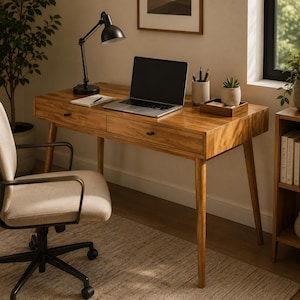 May include: A wooden desk with two drawers and tapered legs, featuring a black desk lamp, a laptop, a notebook, a pen, a pencil holder, and a small wooden tray with a potted succulent. A beige office chair with armrests sits in front.