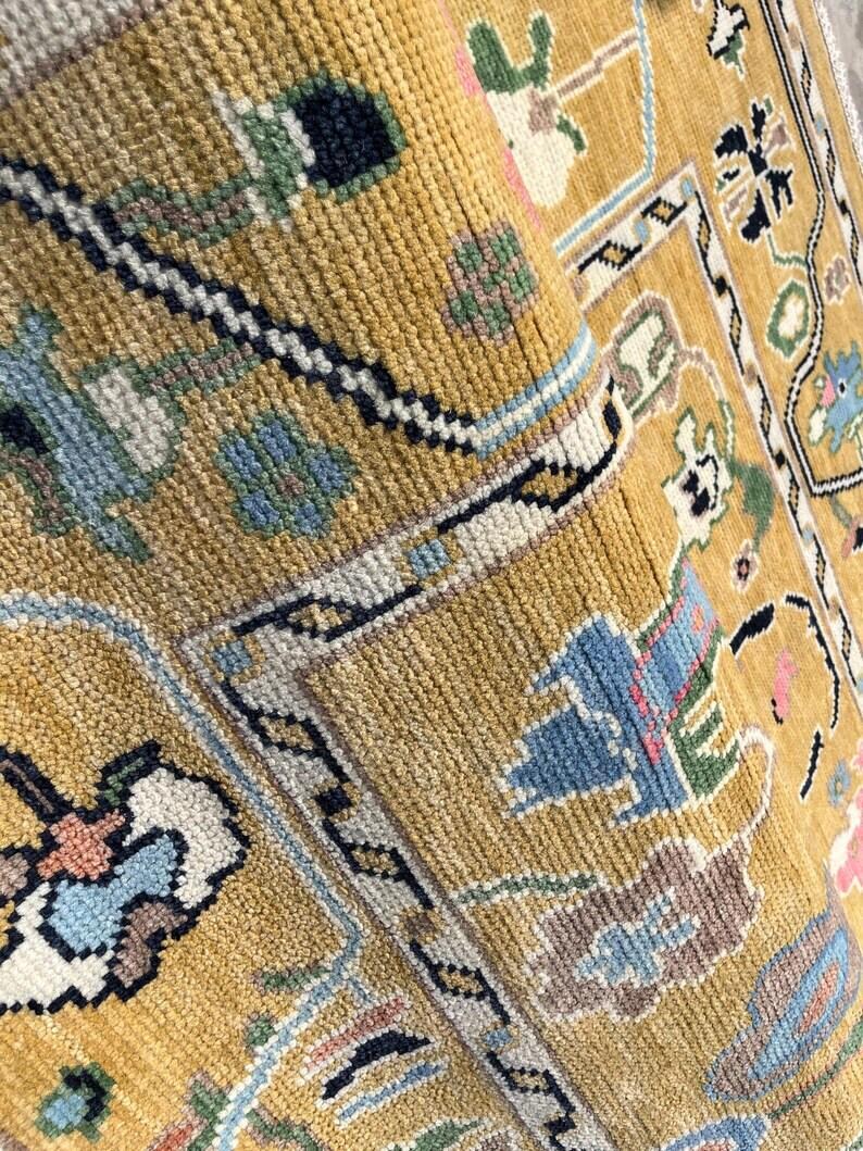 May include: A mustard yellow area rug featuring a dense, knotted pile texture. The surface displays a repeating geometric and floral pattern in shades of light blue, dark navy, white, and soft pink, organized within a structured border design.