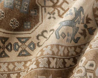 May include: A woven textile rug featuring a detailed pattern in shades of beige, brown, and muted blue. The design includes geometric shapes, stylized floral motifs, and intricate linear borders, all rendered in a dense, textured weave.