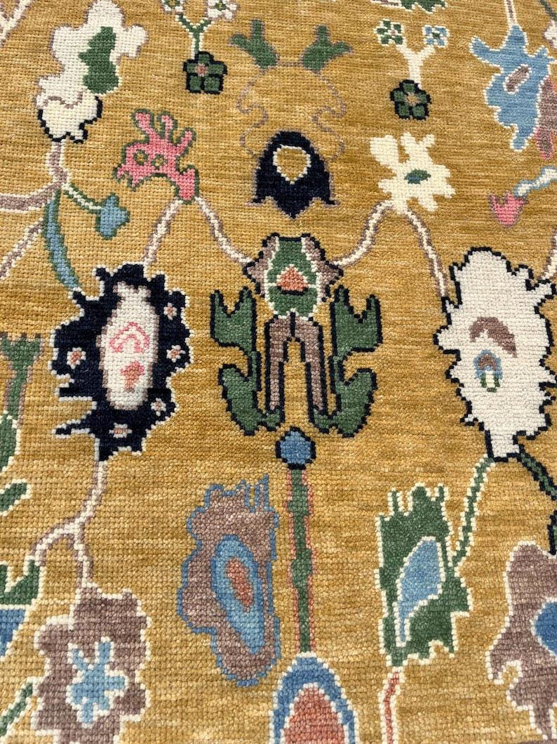 May include: A mustard yellow area rug featuring a woven pattern of stylized floral and botanical motifs in shades of dark blue, forest green, light blue, white, and soft pink. The design consists of interconnected organic shapes and vines.