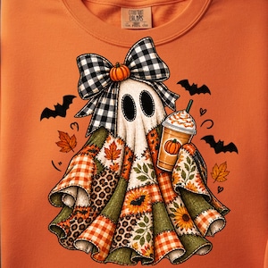 May include: An orange sweatshirt featuring a graphic of a ghost wearing a black and white buffalo plaid bow, holding a pumpkin-topped iced coffee. The ghost is draped in a patchwork-style fabric with autumn leaves, sunflowers, and bats.