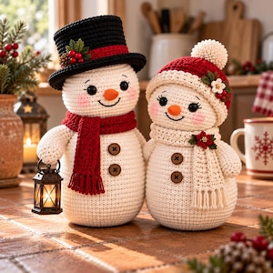以下が含まれることがあります： かぎ針編みの雪だるまのフィギュアが2体並んでいます。左の雪だるまは赤い縁取りの黒いシルクハットと赤いマフラーを身につけ、小さなランタンを持っています。右の雪だるまは白いポンポン付きの赤いニット帽と、花の飾りがついた白いマフラーを身につけています。
