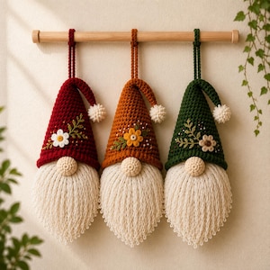 May include: Three hanging crochet gnome ornaments in dark red, orange, and dark green. Each gnome features a pointed hat with a small white pom-pom, a cream-colored yarn beard, a round nose, and embroidered floral details on the front of the hat.