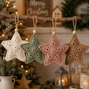 May include: Four star-shaped crochet ornaments hanging from a wooden branch. Each star features a unique color: cream, sage green, dusty rose, and tan. Every ornament includes a small wooden bead at the top and a jute twine loop for hanging.