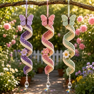 May include: Three hanging spiral ornaments made of crocheted yarn in purple, pink, and light green. Each spiral features a matching crocheted butterfly at the top, a small crocheted flower in the centre, and a clear faceted crystal drop at the bottom.