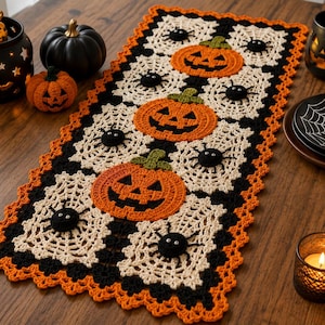 Può includere: Un runner da tavola rettangolare all'uncinetto con un motivo ripetuto di zucche di Halloween arancioni e ragnatele color crema con ragni neri. Il runner presenta un bordo arancione smerlato ed è realizzato in filato nero, arancione e crema.