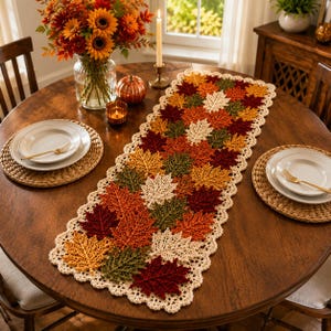 May include: A rectangular crochet table runner featuring a repeating pattern of autumn leaves in shades of red, orange, yellow, and green, finished with a cream-colored scalloped border. The runner is crafted from yarn with visible leaf textures.