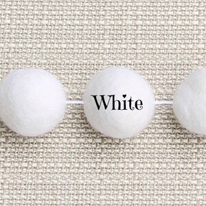 May include: A garland of six white felt balls strung together with white thread. The word "White" is printed below the garland.