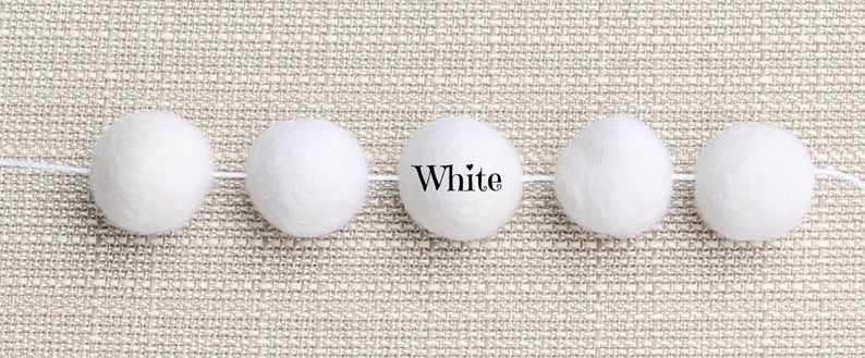 May include: A garland of six white felt balls strung together with white thread. The word "White" is printed below the garland.