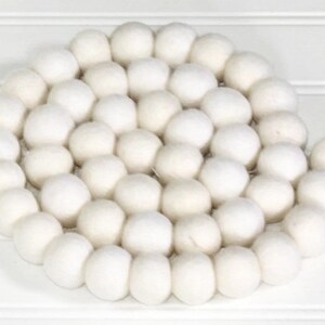 May include: A white felt ball garland, made of many small, round balls strung together. The garland is perfect for adding a touch of whimsy to any space.