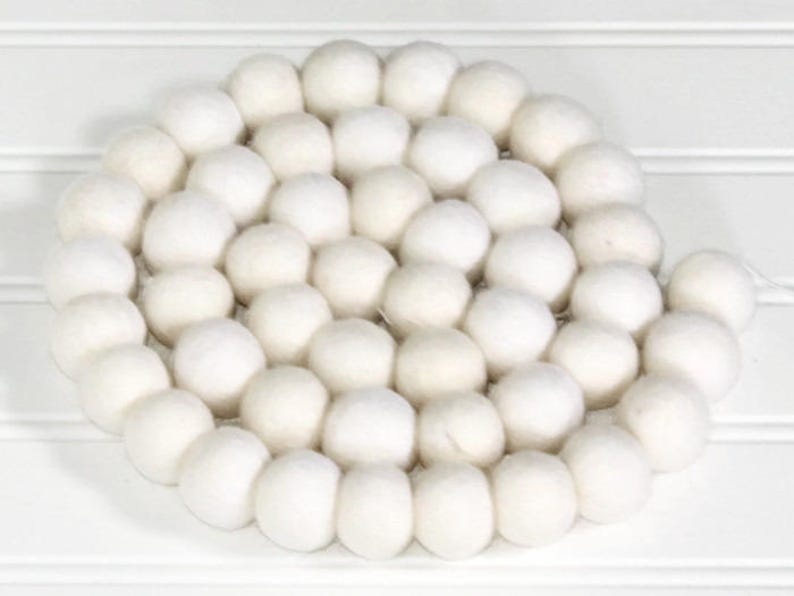 May include: A white felt ball garland, made of many small, round balls strung together. The garland is perfect for adding a touch of whimsy to any space.
