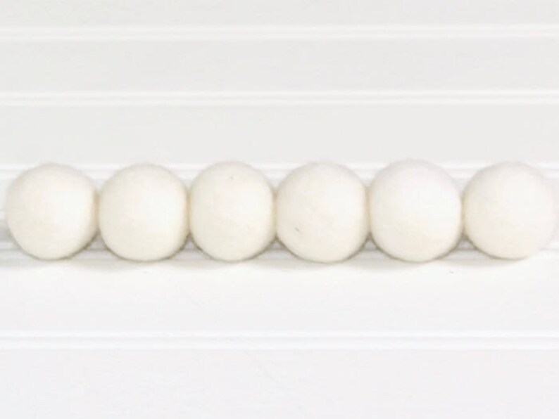 May include: Six white felt balls arranged in a row. The balls are smooth and round.
