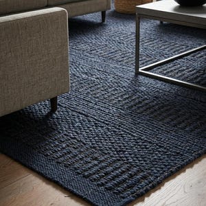 May include: A large, rectangular area rug in a deep navy blue color, featuring a thick, hand-woven texture with a repeating geometric pattern of raised horizontal and vertical lines across its entire surface, creating a dense, tactile appearance.