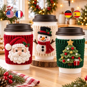 May include: Three white disposable coffee cups with dark brown lids, each featuring a festive crochet cozy. The left cozy is red with a Santa Claus face, the center is cream with a snowman, and the right is green with a Christmas tree.