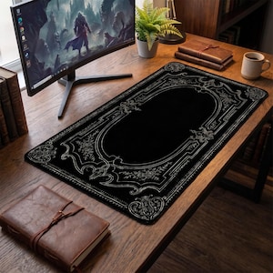 Puede incluir: Una alfombrilla de escritorio rectangular negra con un borde blanco ornamentado con intrincados patrones florales y de volutas. El diseño incluye un marco rectangular central con detalles decorativos en las esquinas para periféricos.