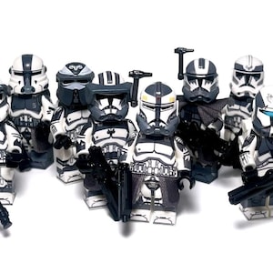 May include: A collection of eight plastic toy soldier minifigures featuring white and dark grey armour with various helmet designs, visors, and attachments. Each figure holds a black plastic blaster accessory, standing in a group formation.