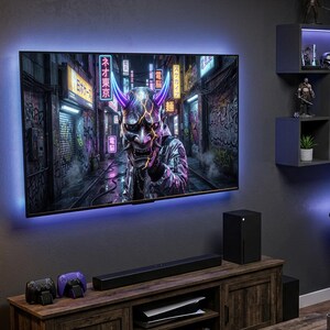 May include: A gaming room featuring a large wall-mounted television displaying a digital oni mask, a wooden media console with a gaming console and soundbar, a desk with a computer monitor, a gaming chair, and wall-mounted shelving with figurines.