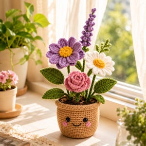 May include: A crochet flower arrangement in a tan pot with a smiling face. The bouquet features a purple daisy with a yellow center, a pink rose, a white daisy with a yellow center, and a tall purple lavender sprig, all with green leaves.