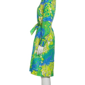 Pode incluir: Um vestido de manga comprida com estampa floral abstrata verde e azul. O vestido tem um cinto de amarra&ccedil;&atilde;o e uma gola.