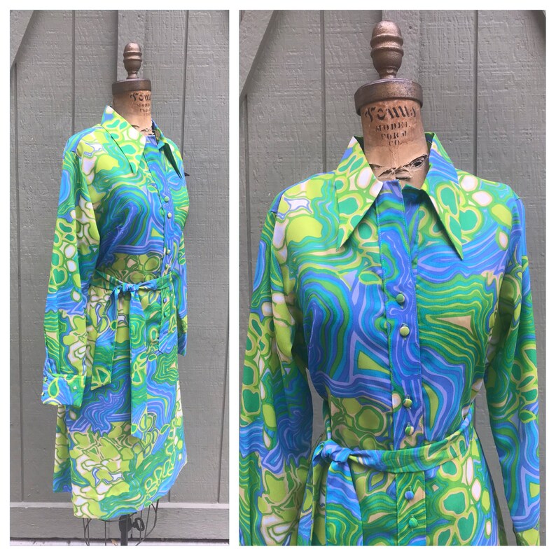 Pode incluir: Um vestido de manga comprida com um padr&atilde;o abstrato de redemoinho verde, azul e branco. O vestido tem um colarinho, fecho de bot&atilde;o e um cinto combinando.