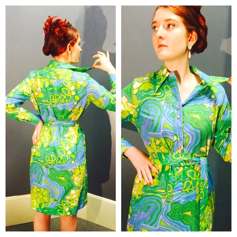 Pode incluir: Um vestido estampado verde, azul e branco com gola e mangas compridas. O vestido tem um cinto e um fecho de bot&atilde;o.