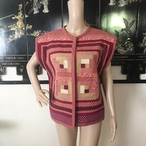 May include: A sleeveless quilted vest with a button-up front. The vest is made of a patchwork of pink and beige fabrics with a geometric pattern.