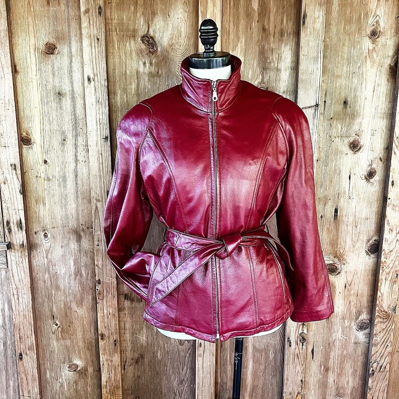 May include: A burgundy leather jacket with a zipper closure and a belt at the waist.
