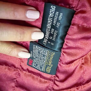 May include: A black and gold care label with the text "Thinsulate Insulation" and instructions for cleaning a garment with Thinsulate insulation. The label states that when dry cleaning is necessary, the garment should be sent to a professional leather cleaner only.