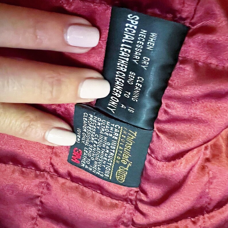 May include: A black and gold care label with the text "Thinsulate Insulation" and instructions for cleaning a garment with Thinsulate insulation. The label states that when dry cleaning is necessary, the garment should be sent to a professional leather cleaner only.