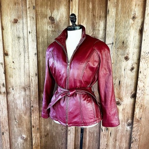 May include: A burgundy leather jacket with a zipper closure and a belt at the waist.