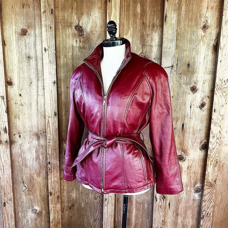 May include: A burgundy leather jacket with a zipper closure and a belt at the waist.