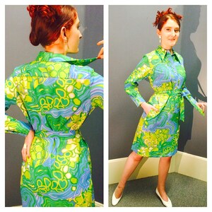 Pode incluir: Um vestido de manga comprida com cinto, estampado em verde, azul e branco. O vestido tem gola e fecho de bot&otilde;es.