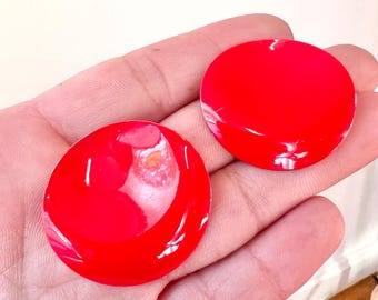 May include: A pair of large, round, red earrings. The earrings are shiny and have a smooth, glossy finish.
