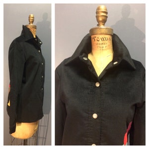 May include: A black corduroy button-up shirt with long sleeves and a pointed collar. The shirt has a small, colorful patch on the left sleeve.