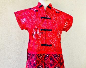 Pode incluir: Um vestido vermelho e preto de manga curta com gola mandarim e estampa floral. O vestido tem fecho de botões na frente e uma faixa contrastante com padrão preto e vermelho na parte inferior.