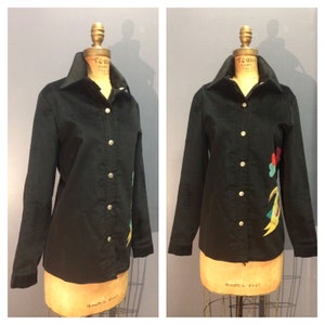 May include: A black corduroy shirt with a colorful embroidered design on the right side. The shirt has a button-up front and long sleeves.