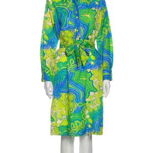 Pode incluir: Um vestido de manga comprida com estampa abstrata verde, azul e branca. O vestido tem gola, fechamento frontal com bot&otilde;es e um cinto de amarra&ccedil;&atilde;o na cintura.