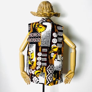 May include: A sleeveless shirt with a colorful geometric and floral pattern in shades of brown, white, yellow, and black. The shirt is made of a lightweight fabric and has a relaxed fit.