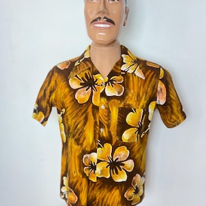 May include: A short-sleeved button-down shirt with a brown and yellow floral pattern. The shirt features a pocket on the chest and is displayed on a mannequin. The floral design includes yellow and white flowers.