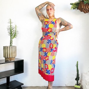 May include: A red, yellow, and blue patchwork dress with a halter neckline. The dress has a geometric pattern and is made of a lightweight fabric.