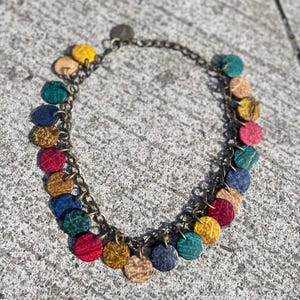 May include: A necklace featuring a bronze-toned metal chain adorned with numerous small, circular, textured discs in a variety of vibrant colors including red, blue, yellow, green, and tan, arranged in a repeating pattern along the entire length.