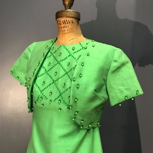 May include: A green dress with a matching jacket, both decorated with green beading in a diamond pattern.