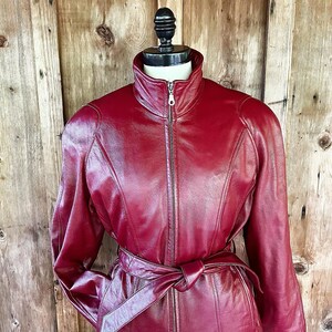 May include: A burgundy leather jacket with a zipper closure and a belt at the waist.