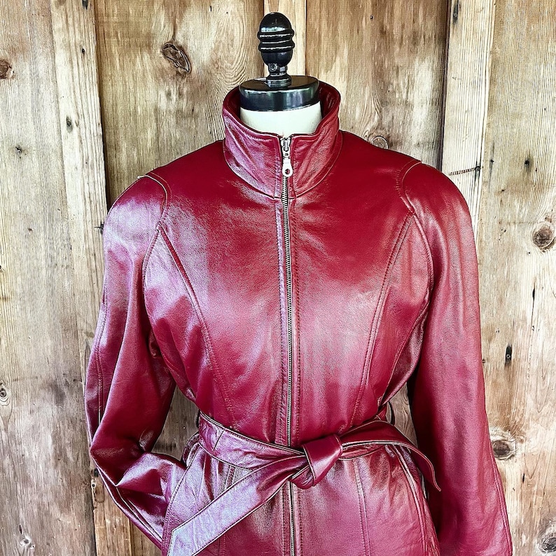 May include: A burgundy leather jacket with a zipper closure and a belt at the waist.
