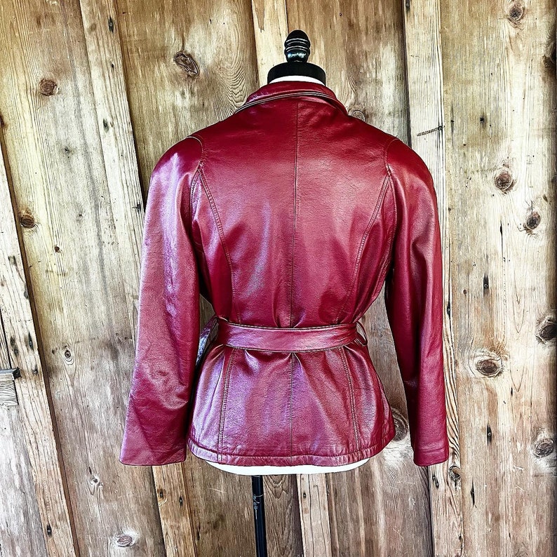 May include: A red leather jacket with a belt. The jacket has a stand-up collar and long sleeves.
