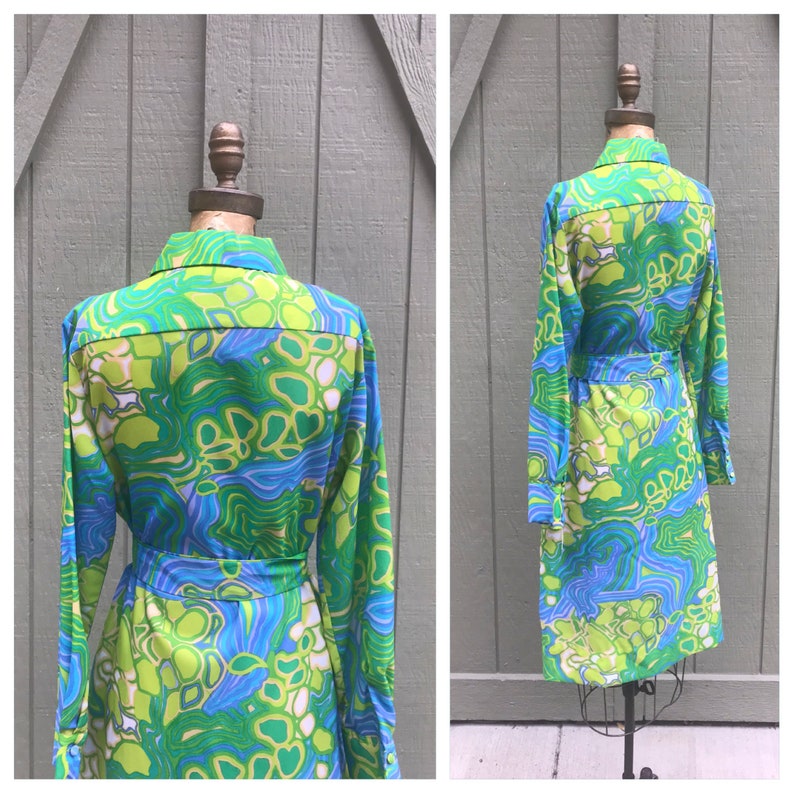 Pode incluir: Um vestido de manga comprida com um padr&atilde;o abstrato verde, azul e branco. O vestido tem gola e cinto.