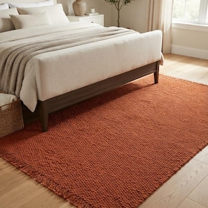 May include: A rectangular area rug in a solid burnt orange color featuring a thick, chunky knit texture and short fringe detailing along the edges. The rug is constructed with a heavy, woven yarn material that creates a distinct, raised surface pattern.