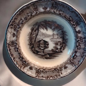 May include: A vintage brown and white ceramic soup bowl with a decorative border and a black and white scene of a building with palm trees and a bridge.