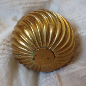 May include: A golden, spiral-shaped object with a circular base. The object has a ridged texture, and the color is a bright, shiny gold. The base is a slightly darker gold color. The object appears to be made of metal.
