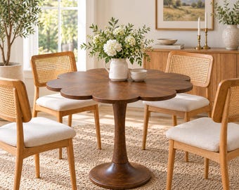 May include: A round, dark brown wooden dining table with a scalloped, flower-shaped edge and a central pedestal base. Four chairs with light beige upholstered seats and natural wood frames featuring woven cane backrests surround the table.